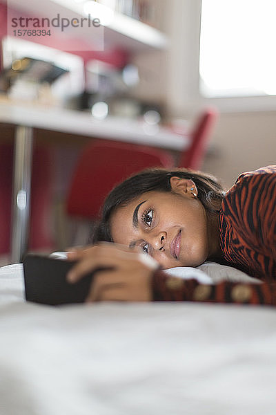 Teenager-Mädchen mit Smartphone spielt auf dem Bett