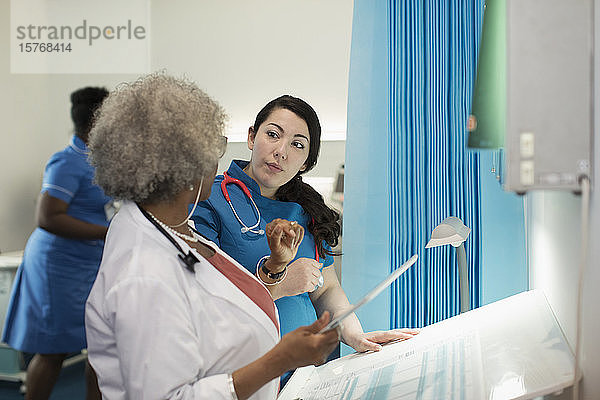 Ärztin und Krankenschwester mit digitalem Tablet im Gespräch im Krankenhauszimmer