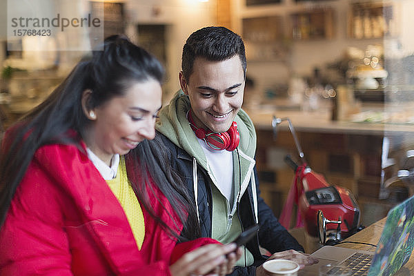 Junges Paar benutzt Smartphone und Laptop in einem Cafe