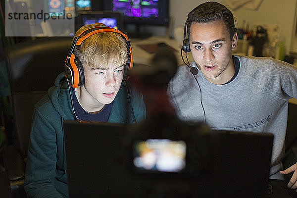 Teenager-Jungen mit Kopfhörern spielen ein Videospiel am Computer in einem dunklen Raum