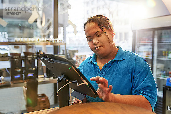 Junge Frau mit Down-Syndrom arbeitet an der Kasse eines Cafés