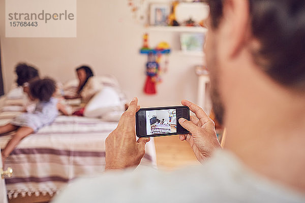 Vater mit Fotohandy fotografiert Familie auf dem Bett