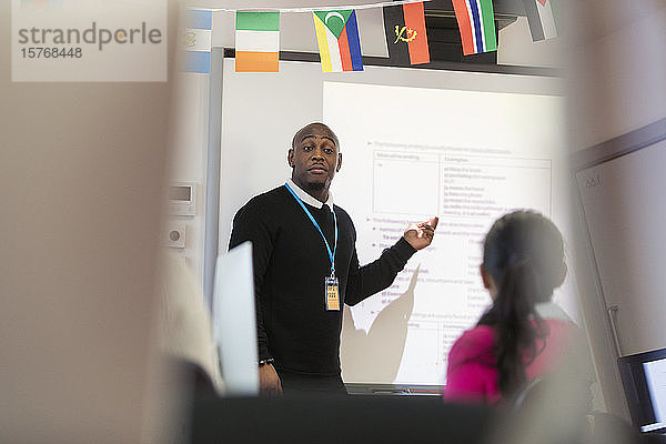 Männlicher Community-College-Lehrer  der eine Unterrichtsstunde an der Projektionsfläche im Klassenzimmer leitet