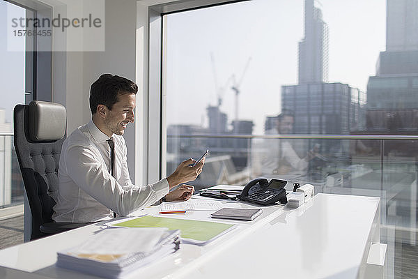 Geschäftsmann mit Smartphone in einem sonnigen  städtischen Büro