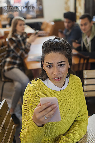 Besorgte junge Frau benutzt ihr Smartphone in einem Café