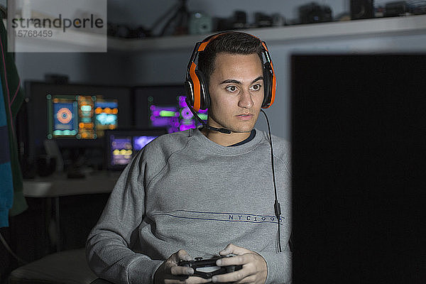 Konzentrierter Jugendlicher mit Headset spielt ein Videospiel am Computer in einem dunklen Raum