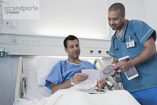 Männlicher Patient zeigt einer Krankenschwester im Krankenhauszimmer eine Grußkarte