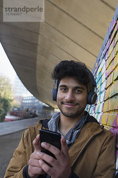 Porträt eines lächelnden jungen Mannes  der mit Kopfhörern und mp3-Player Musik hört