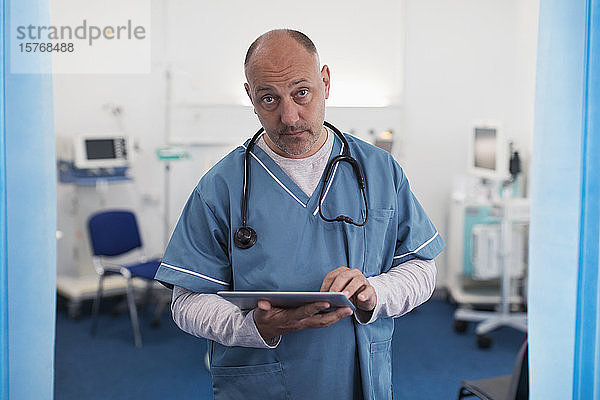 Porträt eines zuversichtlichen  ernsten männlichen Arztes  der ein digitales Tablet in einem Krankenhauszimmer benutzt