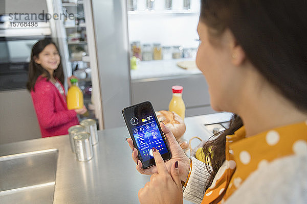 Mutter nutzt Smartphone-App  um Lebensmittel im Kühlschrank zu verfolgen und beobachtet Tochter