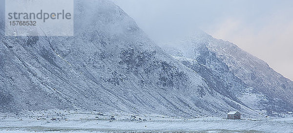 Schneebedeckter Berg und abgelegene Hütte Flakstad Lofoten Norwegen