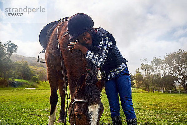 Glückliches Mädchen umarmt Pferd in ländlichem Gras Paddock