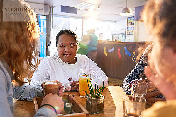 Lächelnde junge Frau mit Down-Syndrom im Gespräch mit Freunden in einem Café