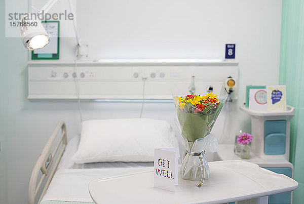 Blumenstrauß und Gute Besserung -Grußkarte auf einem Tablett in einem leeren Krankenhauszimmer