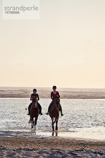 Junge Frauen beim Reiten in der Meeresbrandung