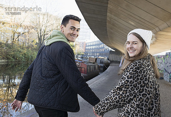 Porträt eines glücklichen jungen Paares  das sich an den Händen hält und am Kanal entlang geht