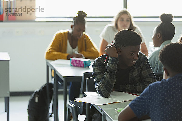 Gymnasiasten machen Hausaufgaben und unterhalten sich an Tischen im Klassenzimmer