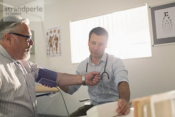 Männlicher Arzt prüft den Blutdruck eines älteren Patienten im Untersuchungsraum