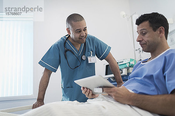 Krankenpfleger im Gespräch mit einem Patienten  der ein digitales Tablet im Krankenhausbett benutzt