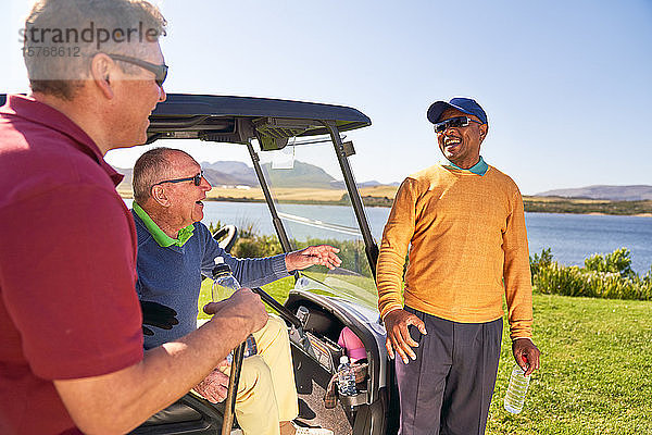 Männliche Golffreunde unterhalten sich und lachen am Golfwagen
