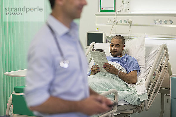 Männlicher Patient liest Zeitung und ruht sich im Krankenhauszimmer aus