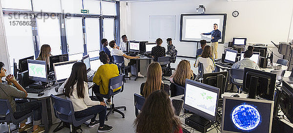 Schüler der Mittelstufe benutzen Computer und beobachten den Lehrer auf der Projektionsfläche im Klassenzimmer