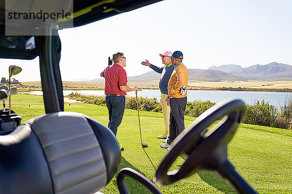 Männliche Freunde unterhalten sich vor einem Golfwagen auf einem sonnigen Golfplatz