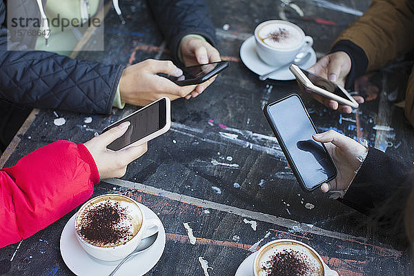 Freunde benutzen Smartphones und trinken Cappuccino am Kaffeetisch