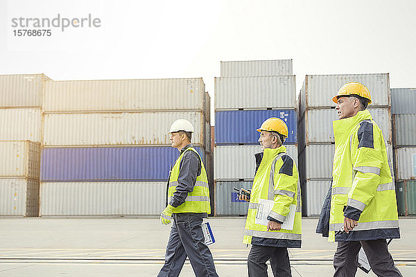 Dockarbeiter gehen entlang von Frachtcontainern auf einer Werft