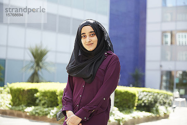 Porträt selbstbewusste junge Frau im Hidschab vor einem sonnigen Gebäude