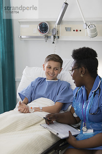 Weibliche Krankenschwester im Gespräch mit einem jungen Patienten im Krankenhauszimmer