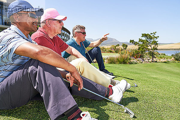 Männliche Golfer ruhen sich im Gras auf einem sonnigen Golfplatz aus