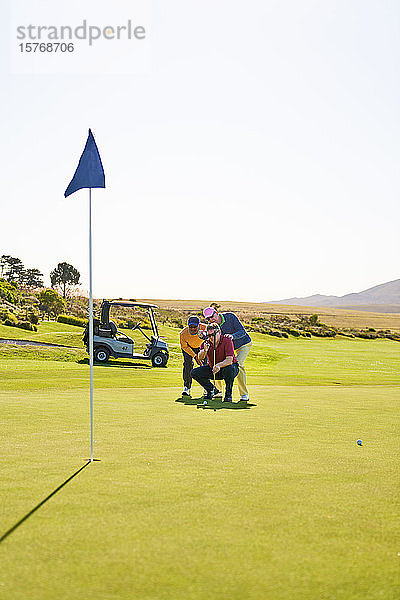 Männliche Golfer planen einen Putt auf dem sonnigen Putting Green eines Golfplatzes