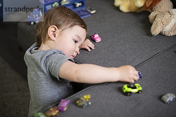 Neugierige niedliche Kleinkind Mädchen spielen mit Spielzeugautos auf dem Sofa