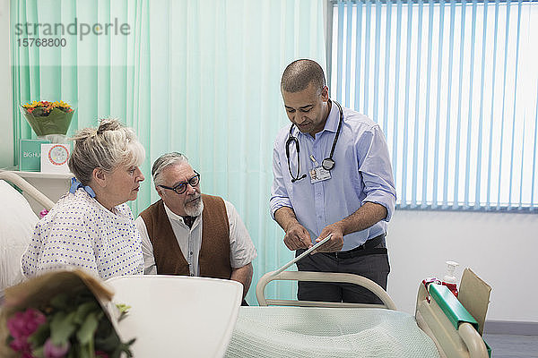 Arzt mit digitalem Tablet bei der Visite  Gespräch mit älterem Ehepaar im Krankenhauszimmer