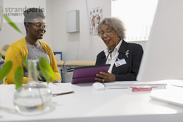 Ärztin mit digitalem Tablet  die sich mit einem Patienten in einer Arztpraxis trifft