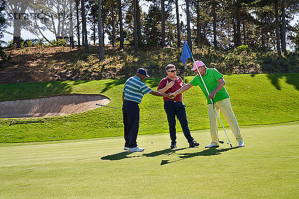 Männliche Golfer beim Händeschütteln auf dem sonnigen Putting Green eines Golfplatzes