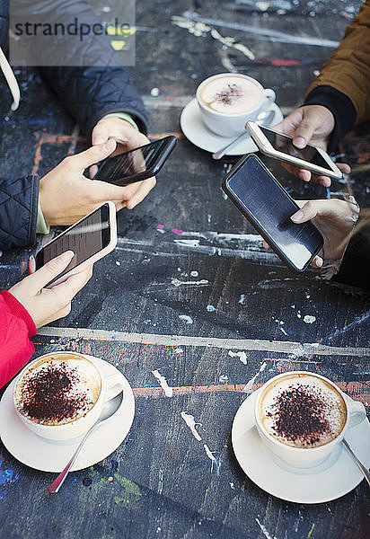 College-Studenten benutzen Smartphones und trinken Cappuccino am Kaffeetisch