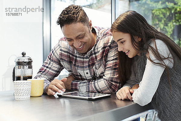 Lächelnder Vater und Tochter benutzen ein digitales Tablet am Küchentisch