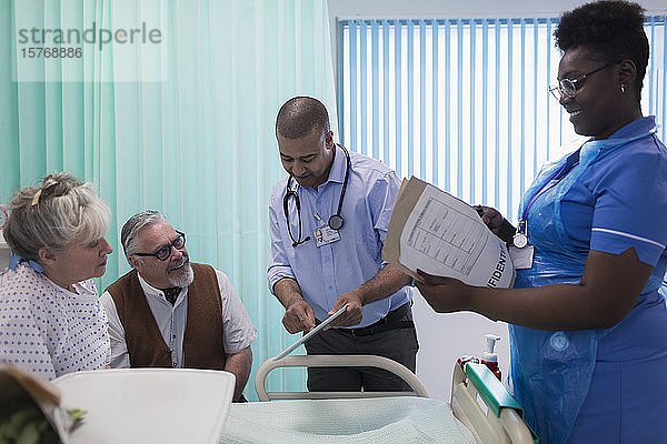 Arzt und Krankenschwester mit digitalem Tablet und Krankenblatt bei der Visite  Gespräch mit älterem Ehepaar im Krankenhauszimmer