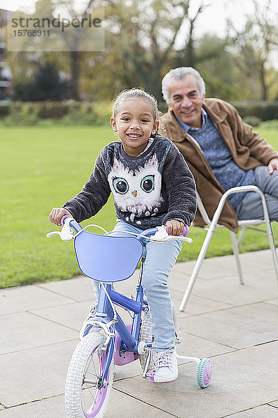 Porträt lächelnde Enkelin auf Fahrrad mit Großvater im Park