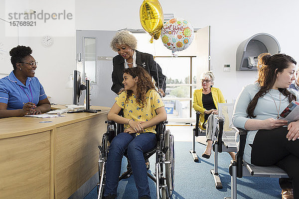 Empfangsdame begrüßt Patientin im Rollstuhl in einer Klinik