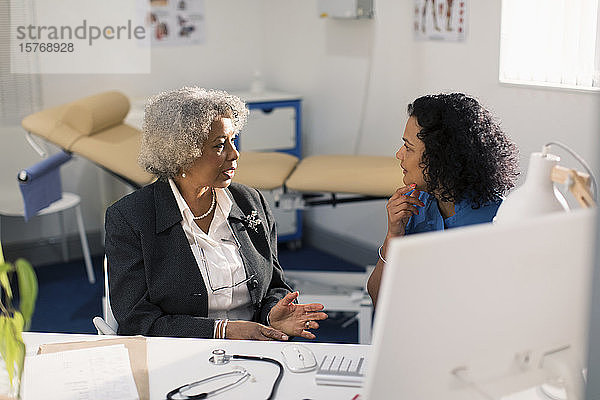 Ärztin im Gespräch mit einem älteren Patienten in einer Arztpraxis