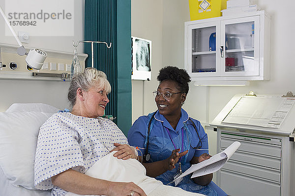 Weibliche Krankenschwester im Gespräch mit einem älteren Patienten im Krankenhauszimmer