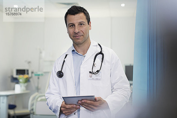 Porträt selbstbewusster männlicher Arzt  der ein digitales Tablet in einem Krankenhauszimmer benutzt