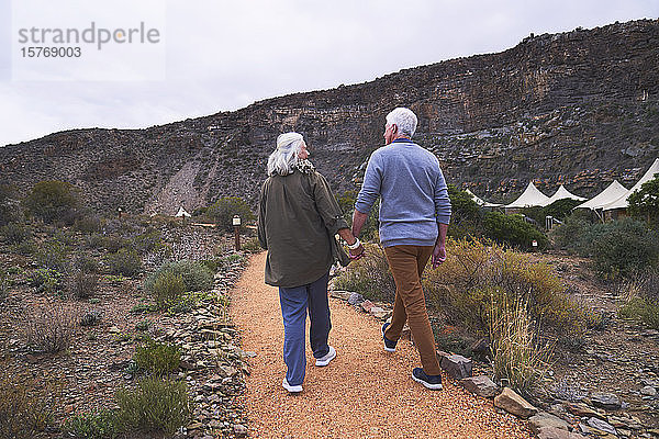 Älteres Paar hält sich auf dem Fußweg vor den Hütten der Safari-Lodge an den Händen