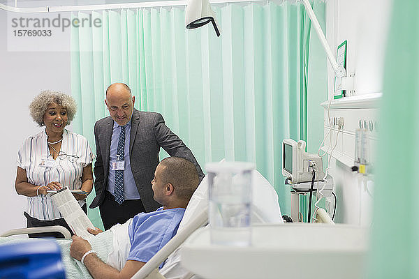 Ärzte bei der Visite  Gespräche mit Patienten  die im Krankenhauszimmer Zeitung lesen