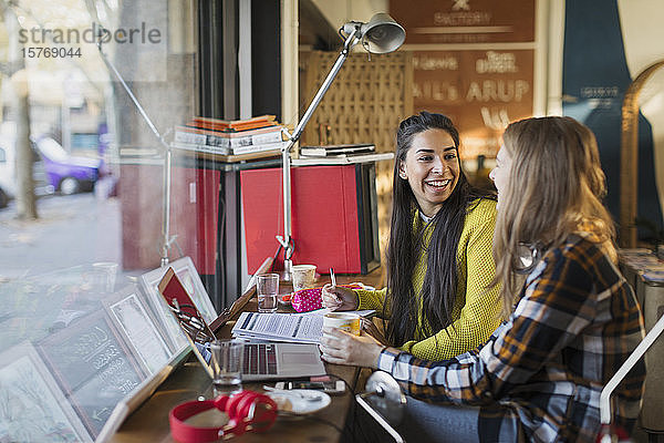 Lächelnde Studentinnen studieren am Fenster eines Cafés
