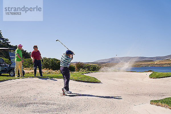 Mann  der aus einem Bunker auf einem sonnigen Golfplatz schießt