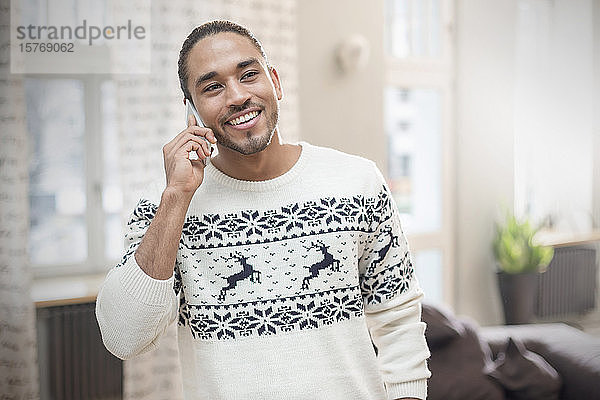 Lächelnder junger Mann im Weihnachtspulli  der mit seinem Handy telefoniert